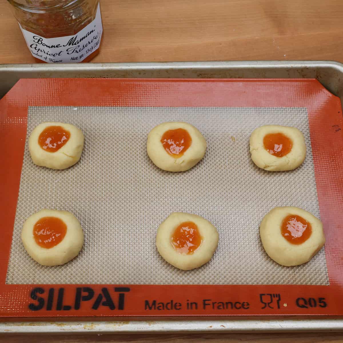 spooning jam into the center of six cookies on a baking sheet.