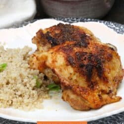 two baked chicken thighs on a white plate next to a side of cooked quinoa.