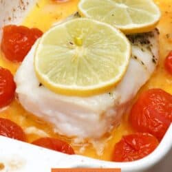 an oven baked cod fillet topped with butter and lemons and surrounded by cherry tomatoes in a baking dish.