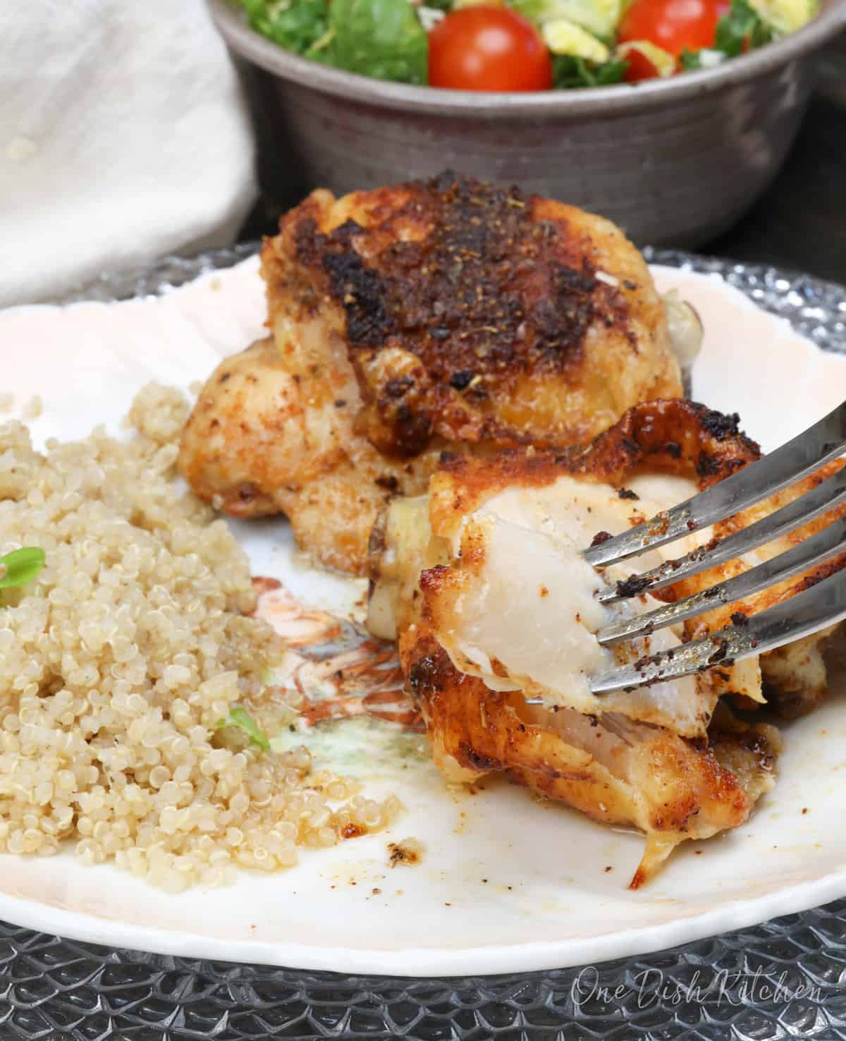 two baked chicken thighs on a plate with a fork pulling off some of the meat.