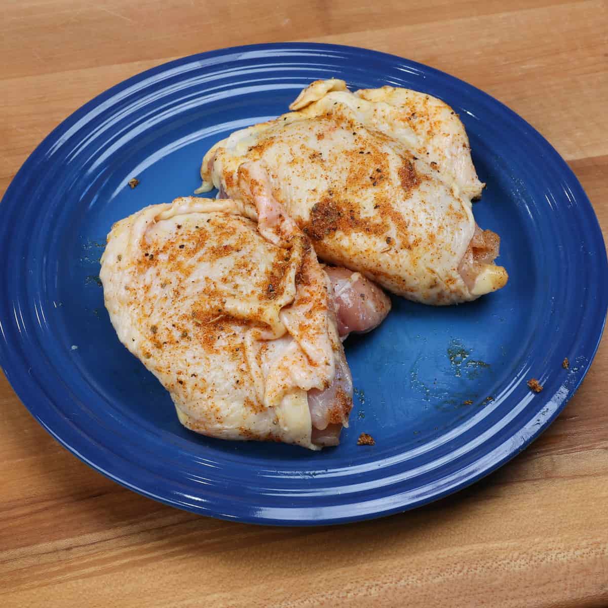 two chicken thighs coated in seasonings on a blue plate.