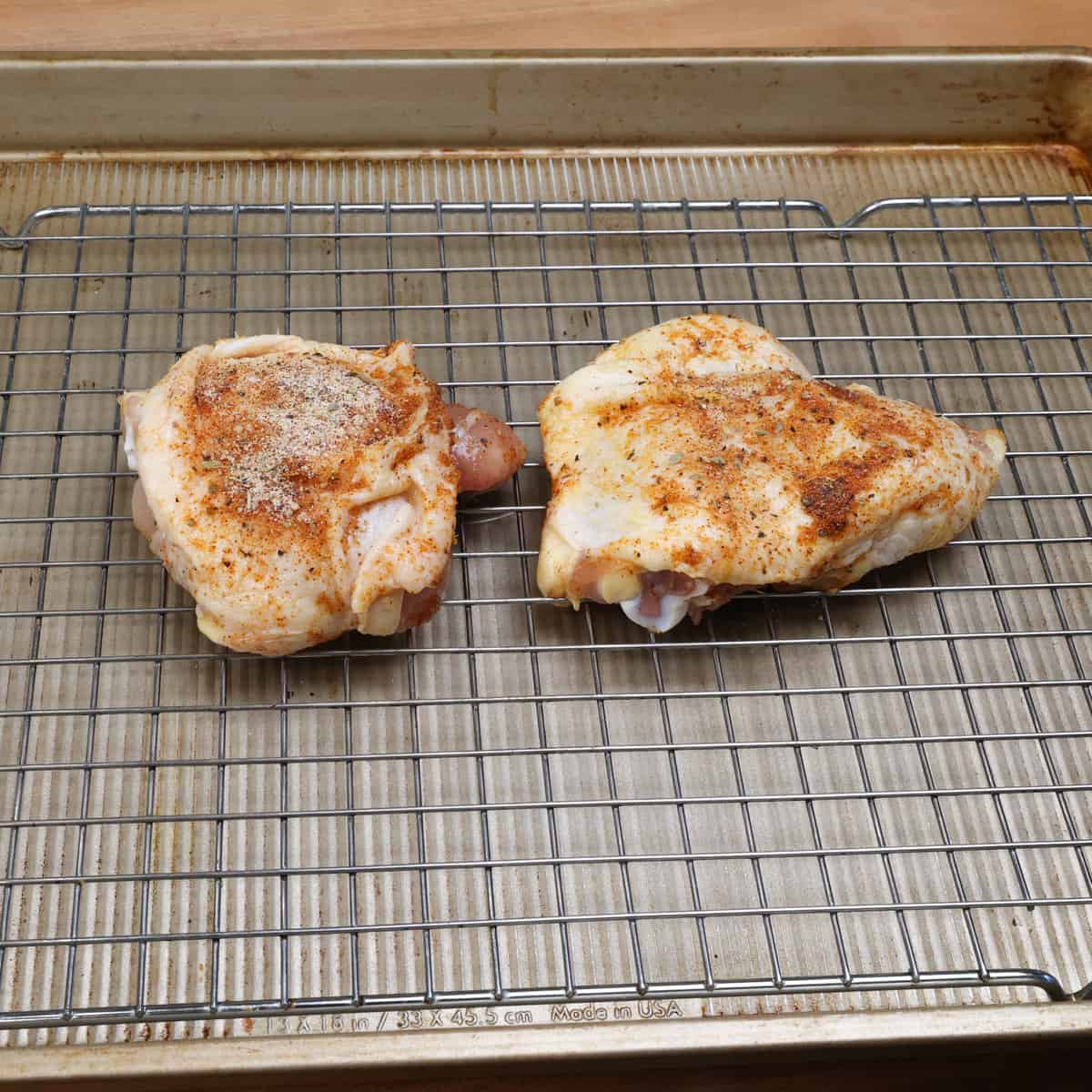 two chicken thighs on a rack over a baking sheet.