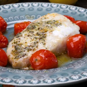 a single cod fillet baked alongside tomatoes and lemons on a blue plate.
