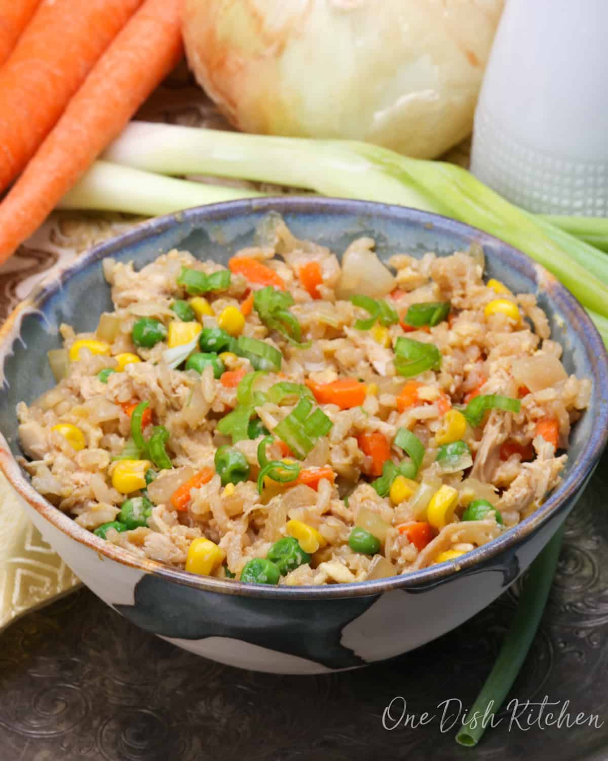 a bowl of chicken fried rice next to carrots and celery and a brown napkin.