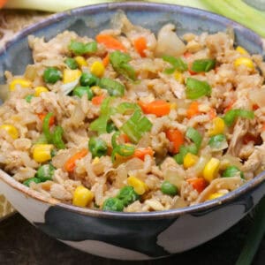 a bowl of chicken fried rice next to carrots and celery and a brown napkin.