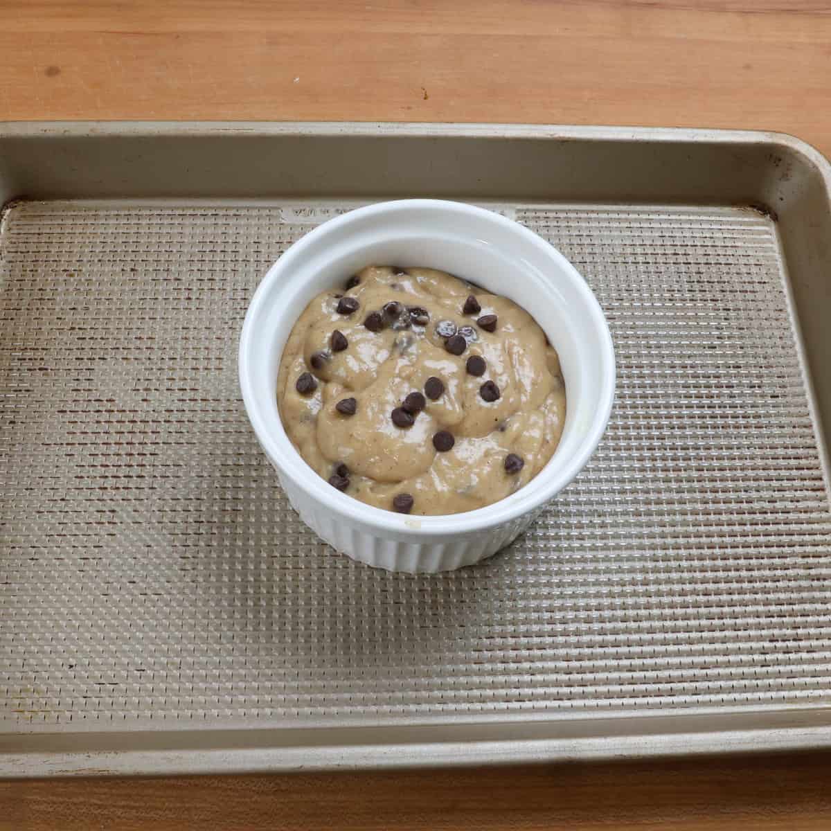 a small unbaked chocolate chip banana bread in a white ramekin on a baking sheet.