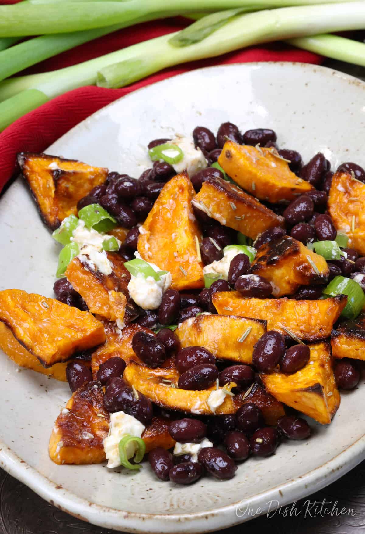 roasted sweet potatoes and black beans topped with crumbled goat cheese on a white plate next to a red napkin.