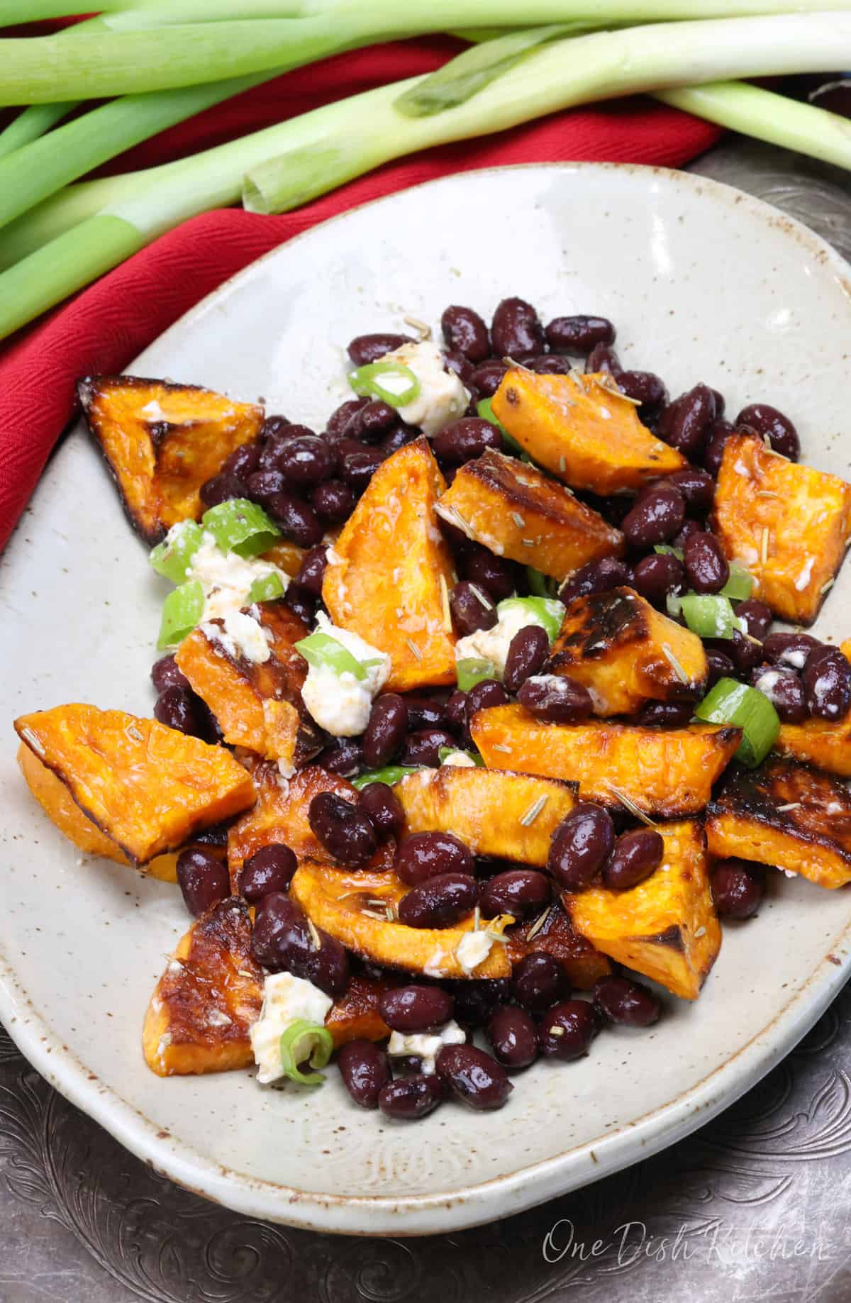 a sweet potato and black bean salad on a white plate topped with goat cheese and green onions.