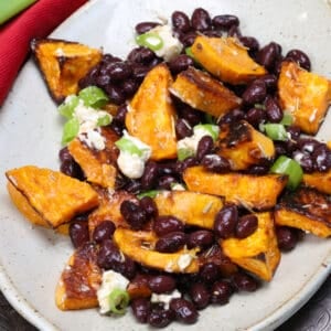 a sweet potato and black bean salad on a white plate topped with goat cheese and green onions.