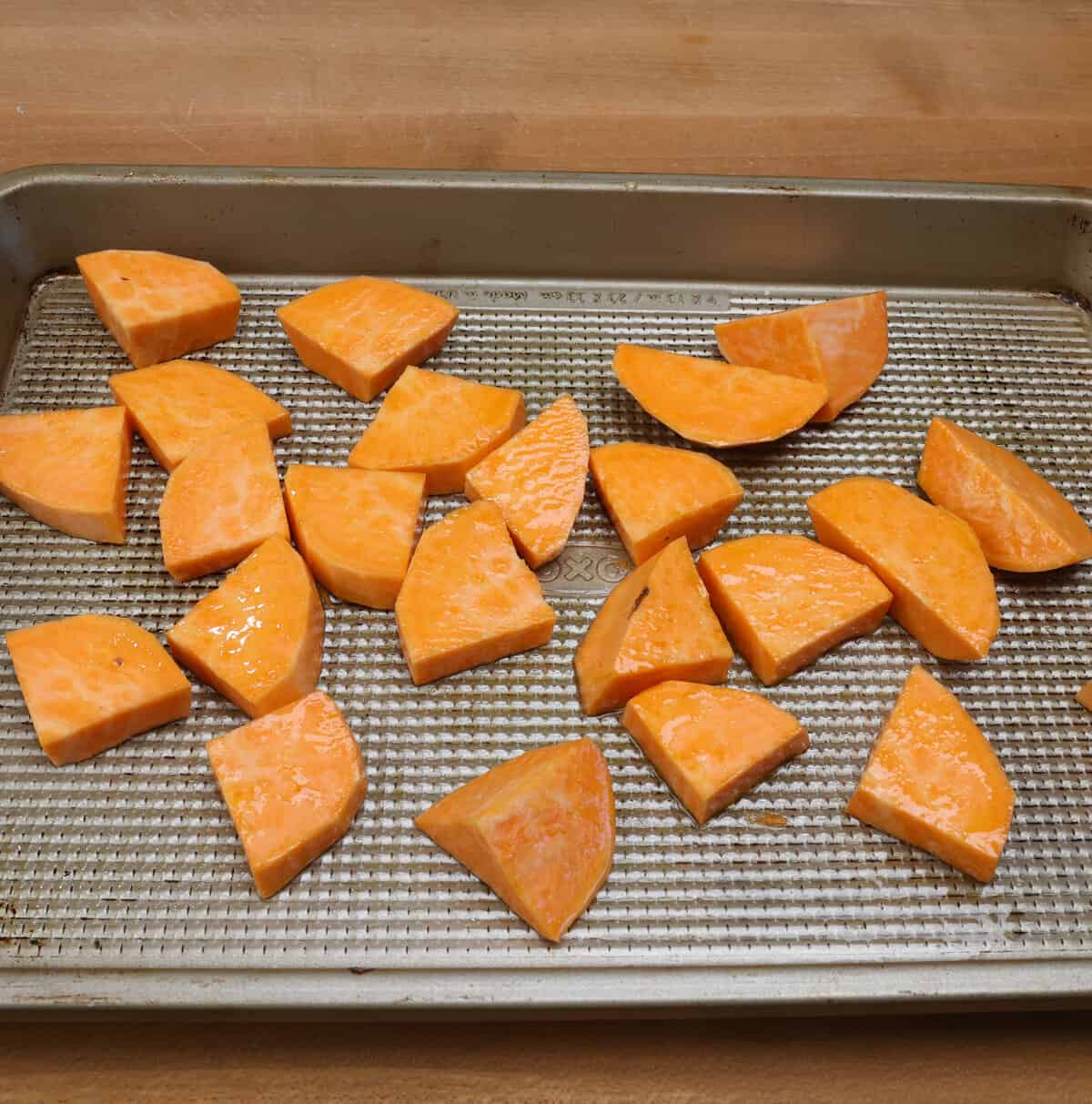 Cubed sweet potatoes tossed with olive oil and seasonings on a rimmed baking sheet.