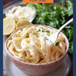 a pink bowl filled with fettuccine alfredo next to sliced lemons.