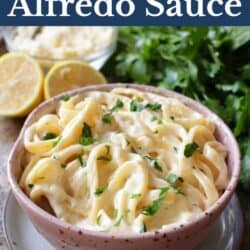 a pink bowl filled with fettuccine alfredo next to sliced lemons.