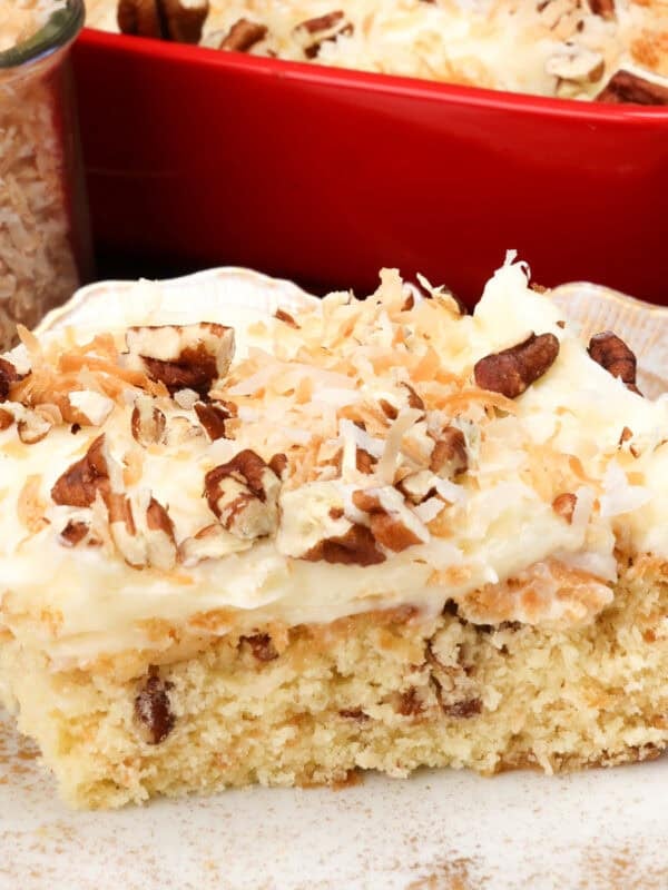 a slice of italian cream cake on a white plate next to a jar of toasted coconut.