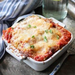 Baked lasagna with melted cheese on top in a small white baking dish.