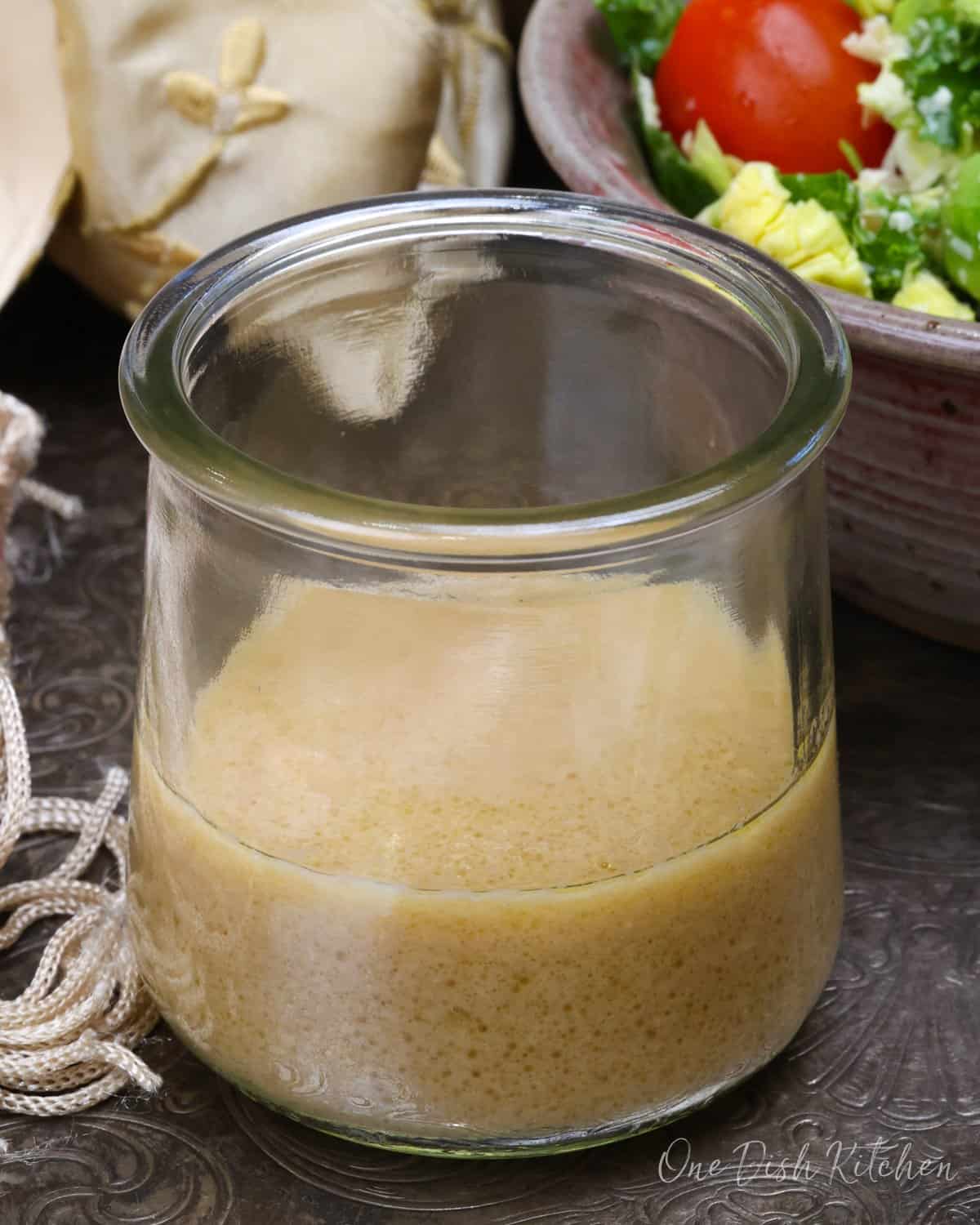 a small batch of vinaigrette next to a green salad.