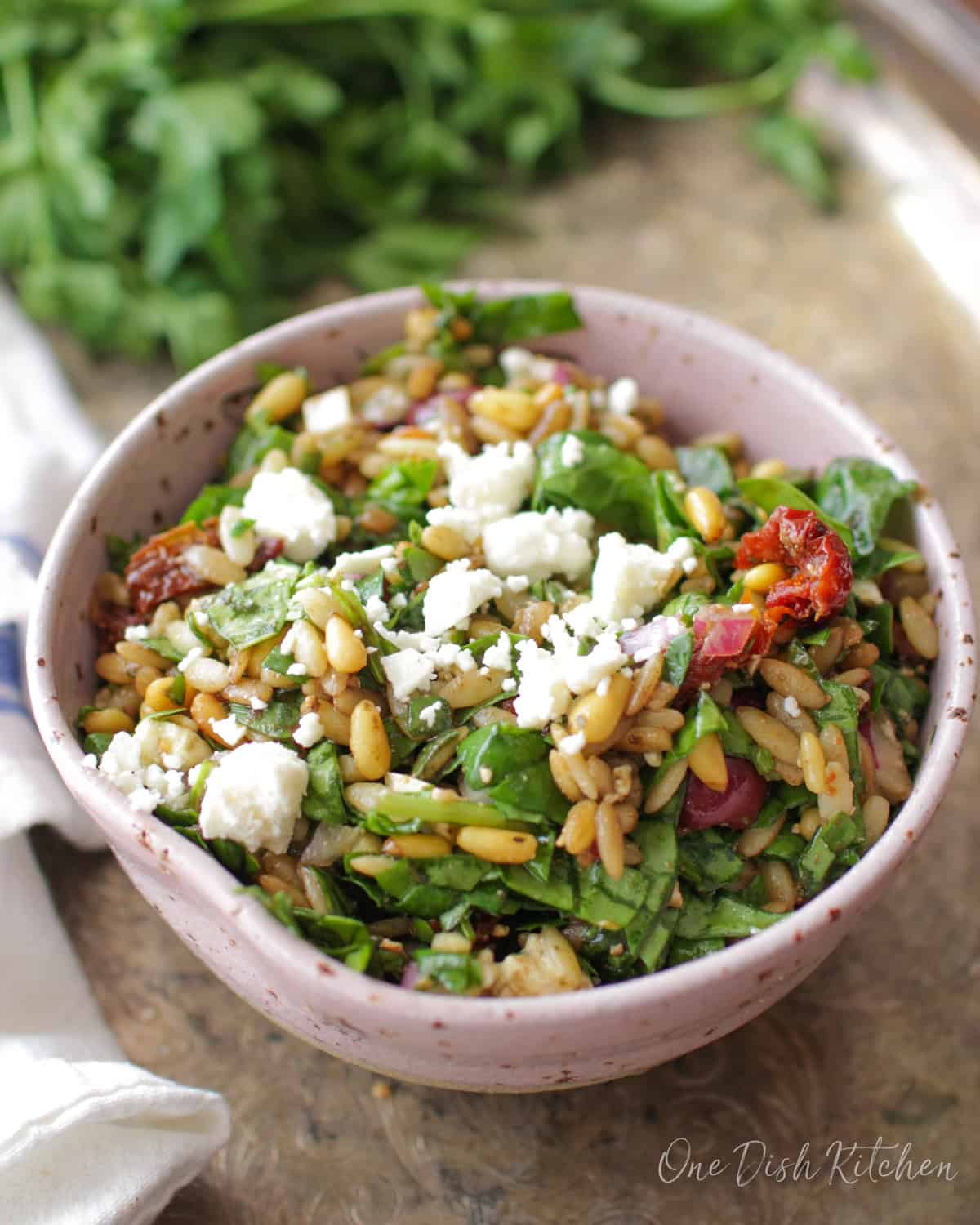 a spinach and orzo salad in a pink bowl on a silver tray.