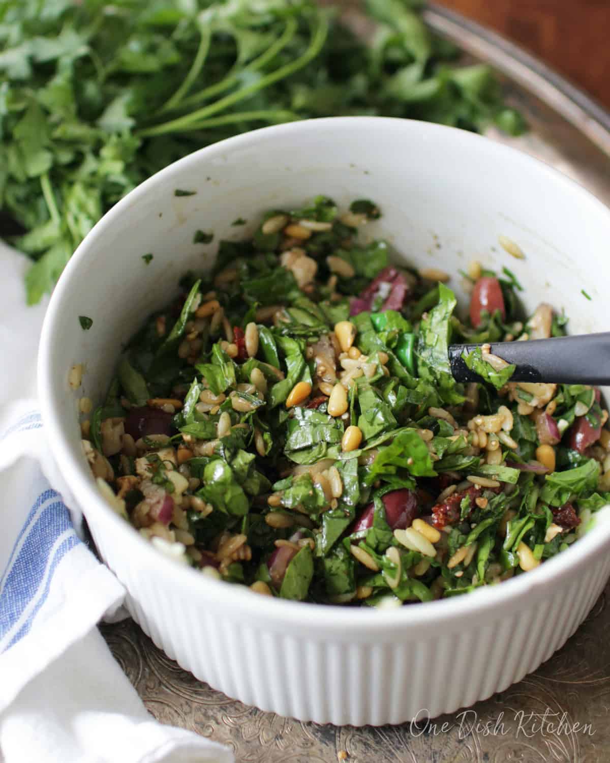 Mixing orzo, spinach, sun-dried tomatoes, onions, kalamata olives, and feta cheese in a bowl.