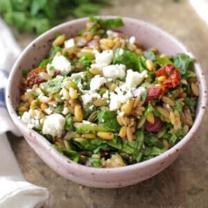 a spinach and orzo salad in a pink bowl on a silver tray.