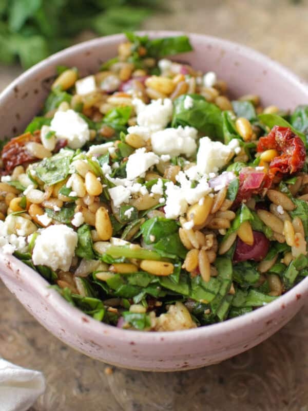 a spinach and orzo salad in a pink bowl on a silver tray.