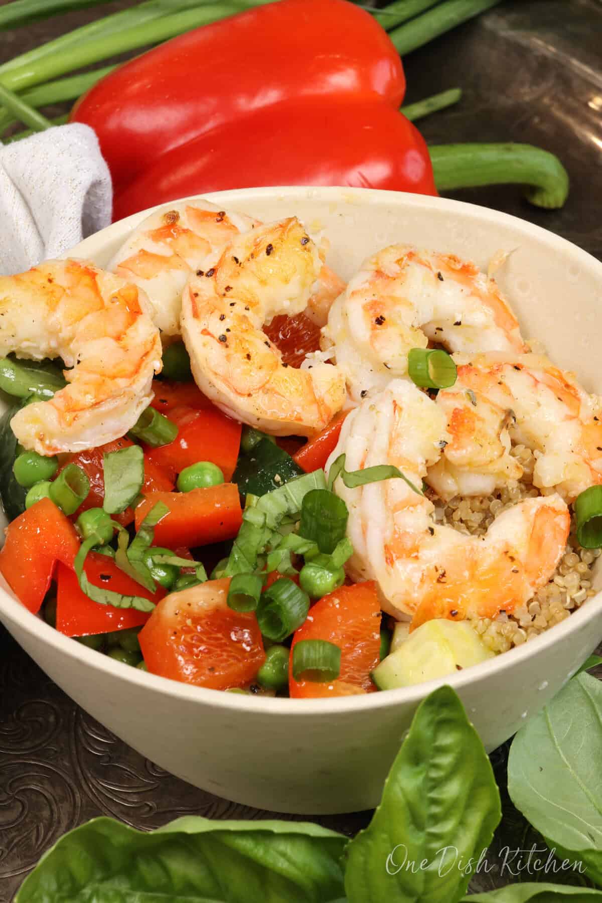 a quinoa bowl topped with cooked shrimp and fresh vegetables.