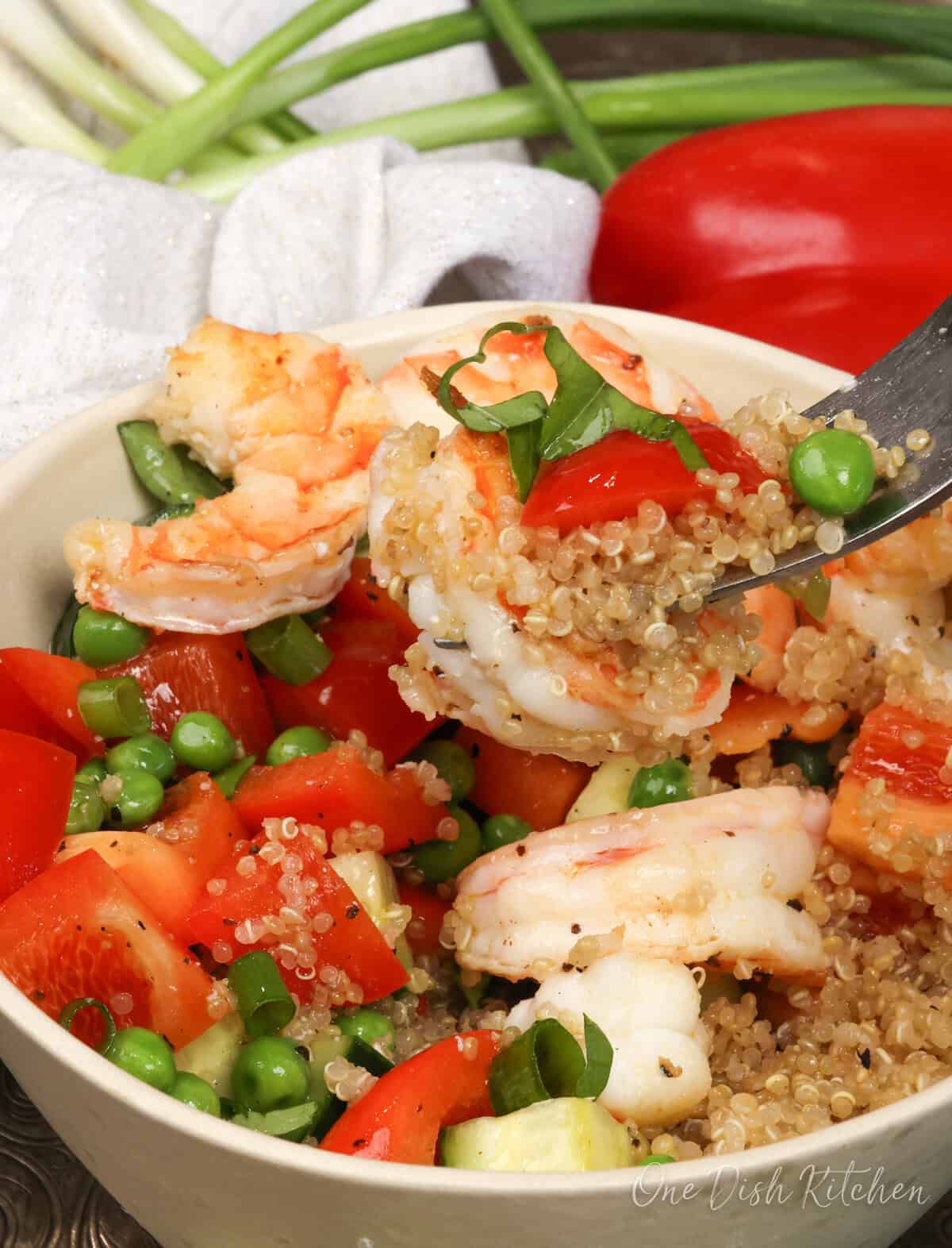 shrimp and quinoa on a fork over a bowl of vegetables and quinoa.