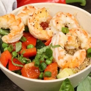 a shrimp quinoa bowl with vegetables on a tray next to fresh basil.