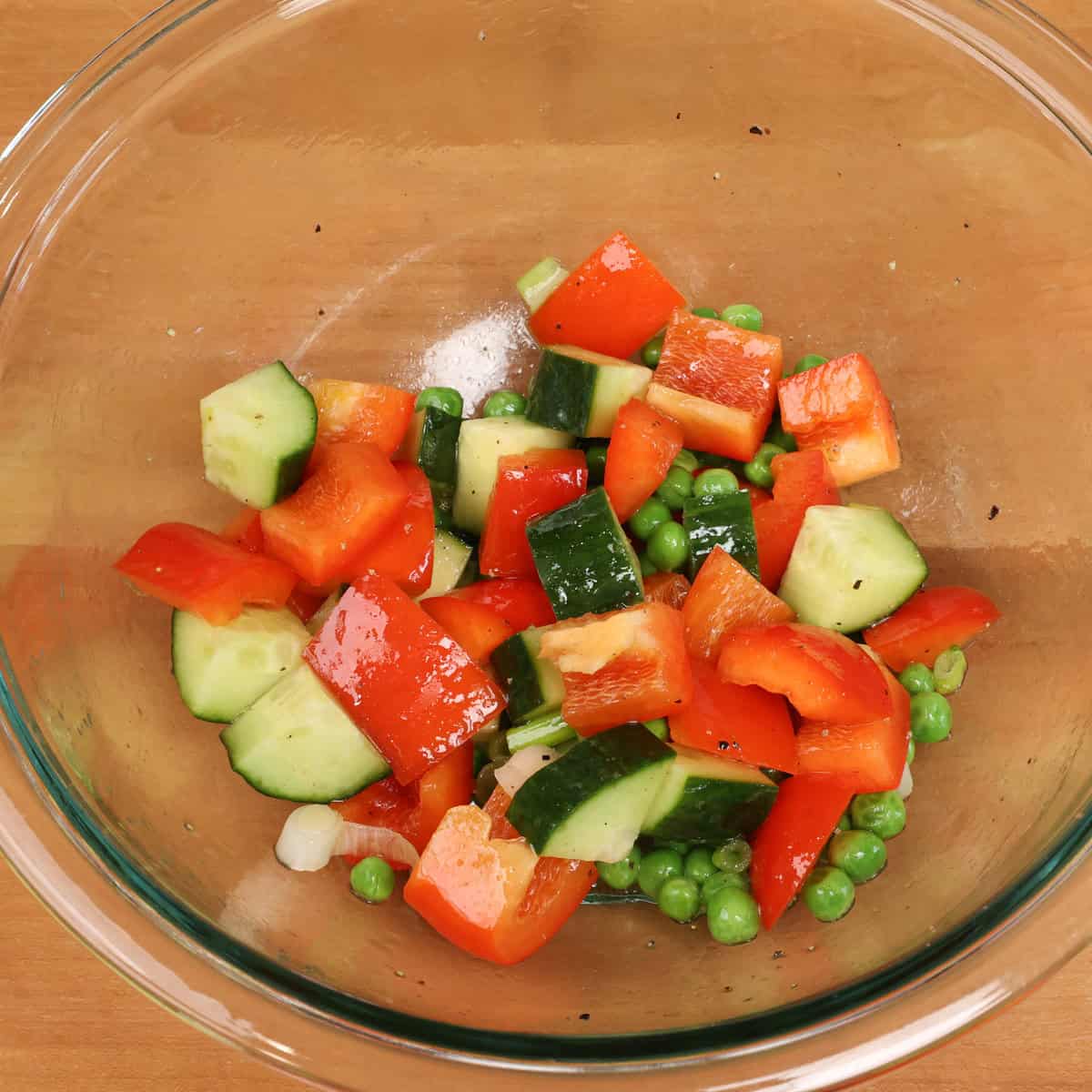 a bowl of chopped bell peppers, cucumbers, and peas.