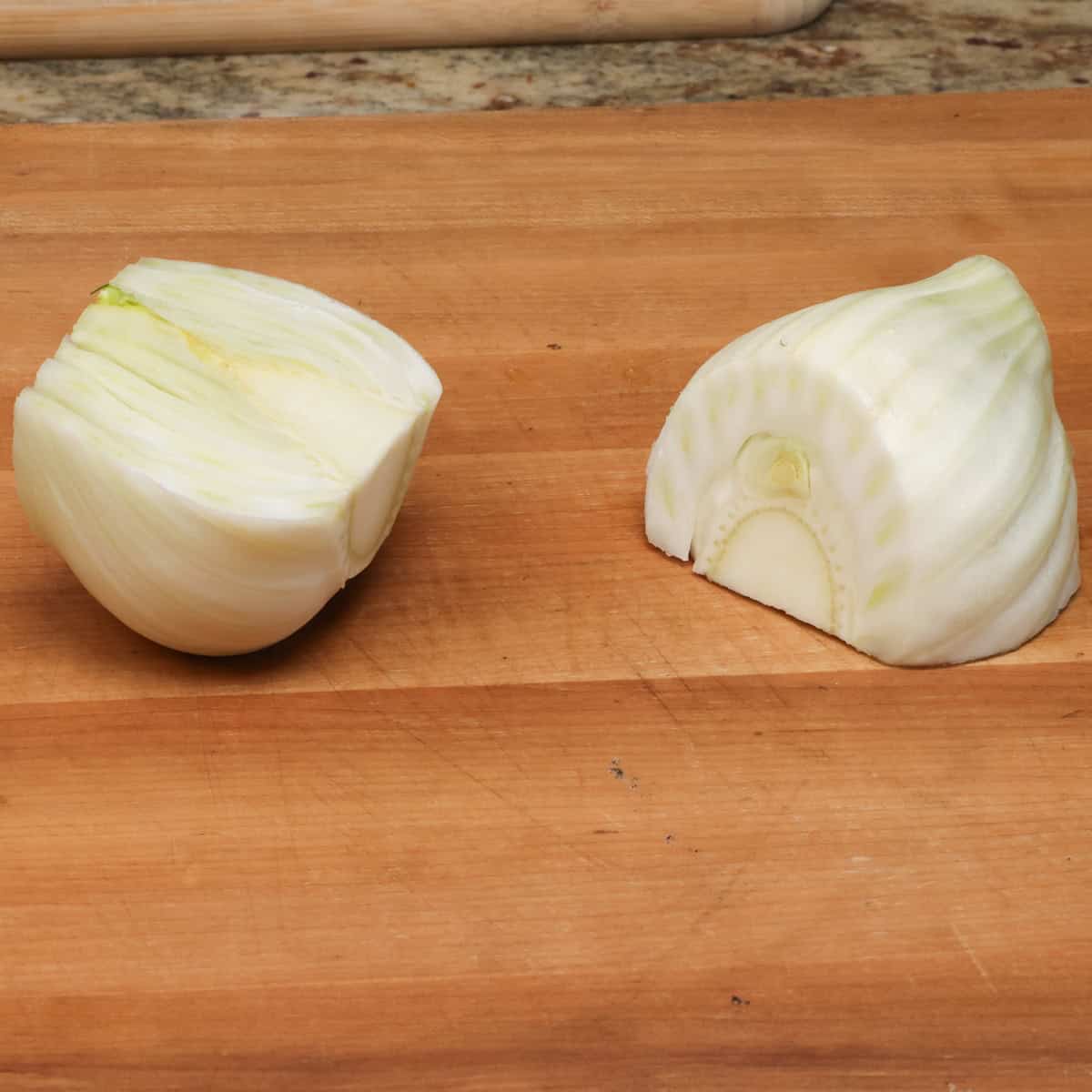a fennel bulb sliced in half on a wooden cutting board.