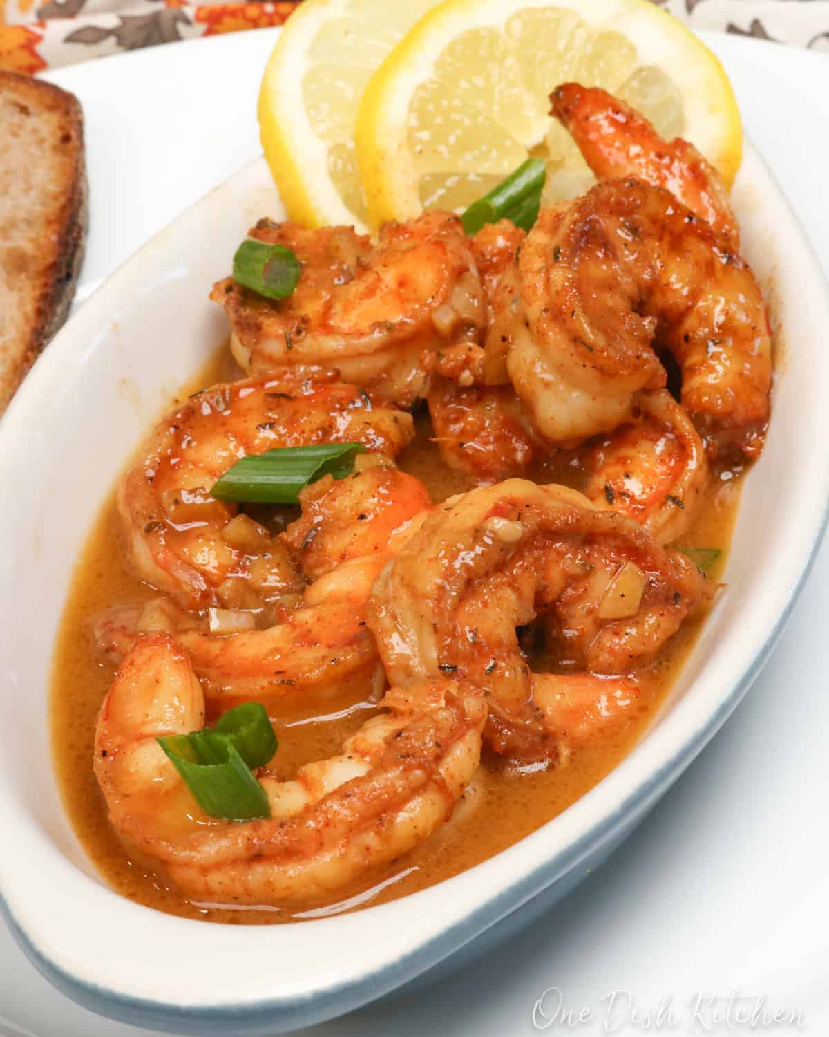 BBQ shrimp in a white bowl topped with sliced green onions and lemon slices.