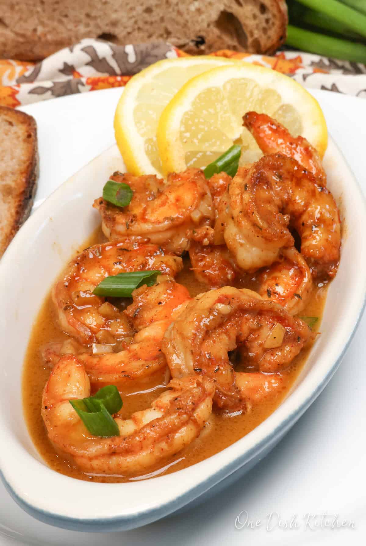 BBQ shrimp in a white bowl topped with sliced green onions and lemon slices.