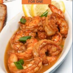 BBQ shrimp in a white bowl topped with sliced green onions and lemon slices.