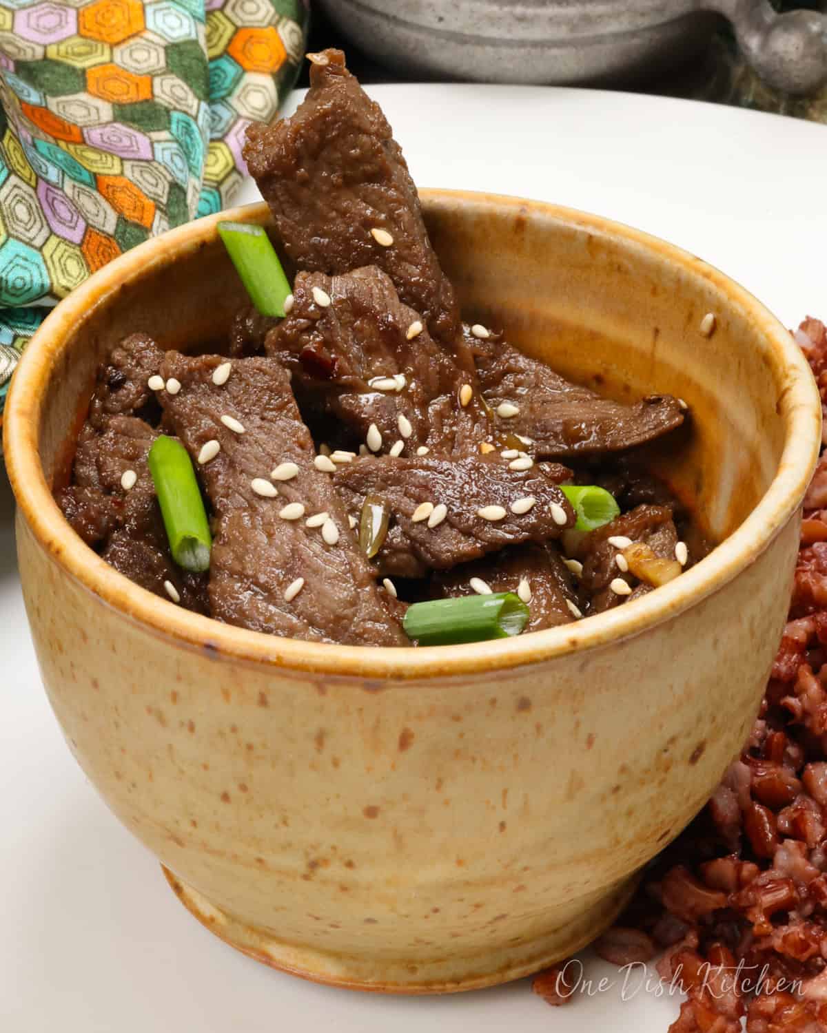 a bowl of beef bulgogi next to a colorful napkin.