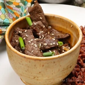 a brown bowl filled with korean beef bulgogi topped with sesame seeds.
