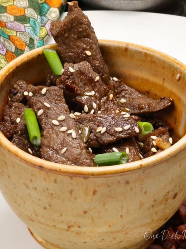 a brown bowl filled with korean beef bulgogi topped with sesame seeds.