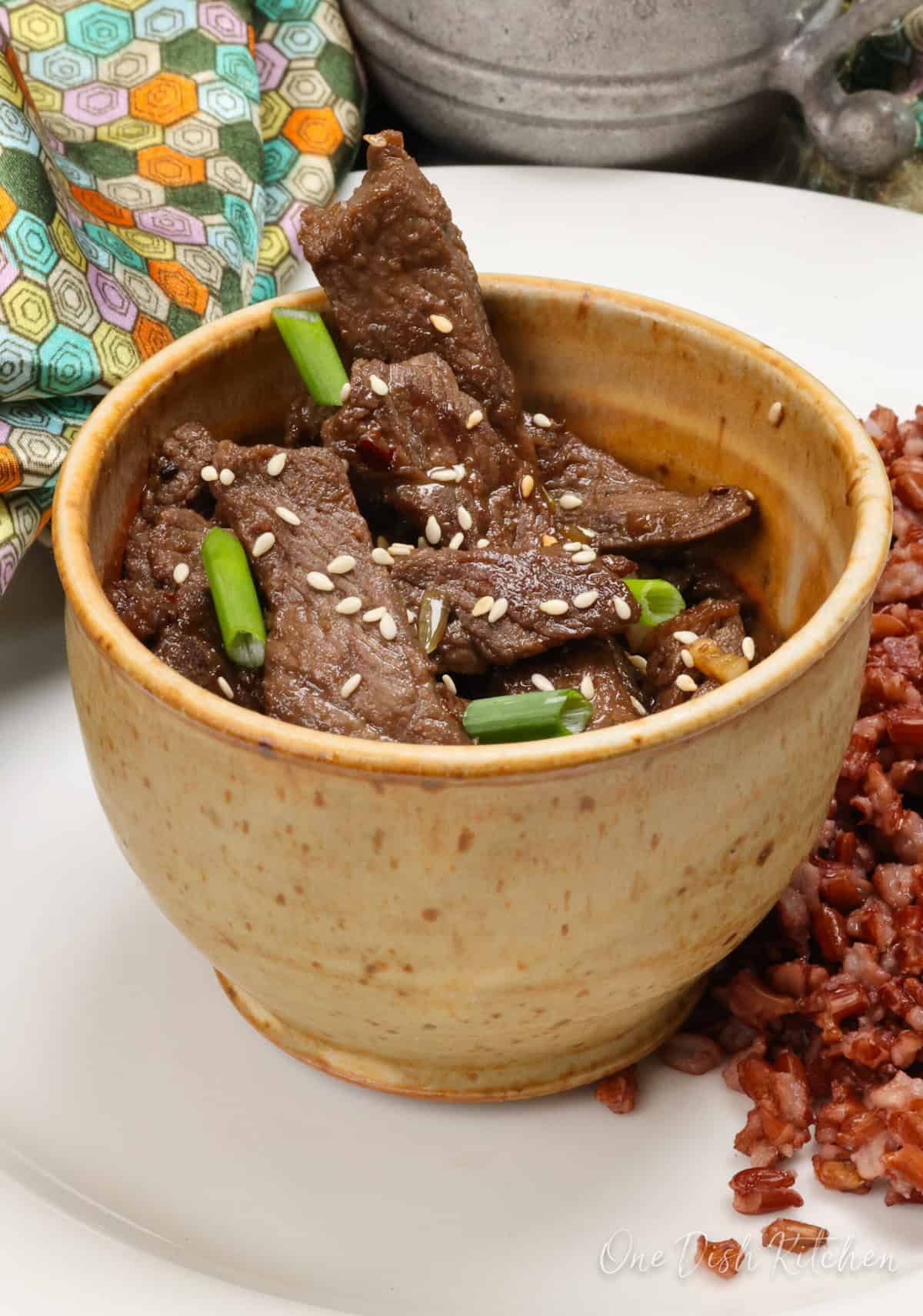 beef bulgogi in a brown bowl served with red rice on the side.
