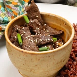 beef bulgogi in a brown bowl topped with sliced green onions and sesame seeds.