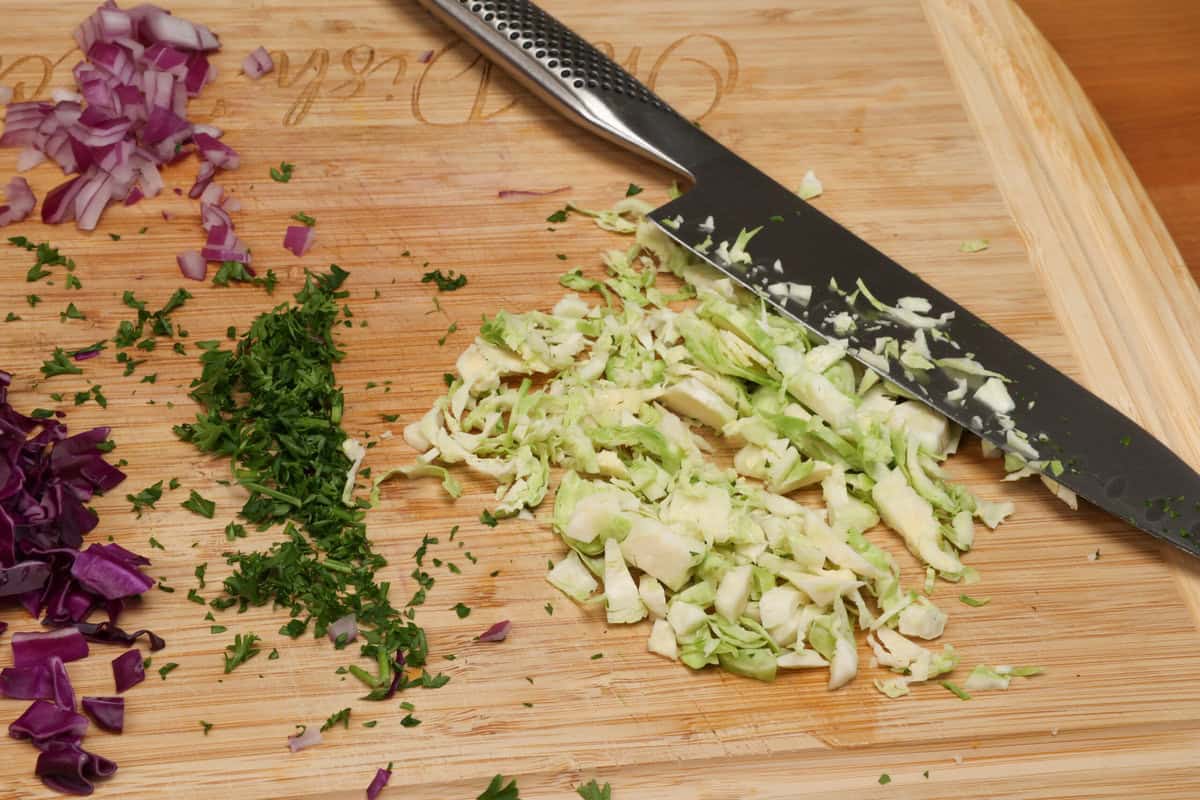 shaved brussels sprouts, chopped parsley and red onions, and thinly sliced cabbage on a cutting board.