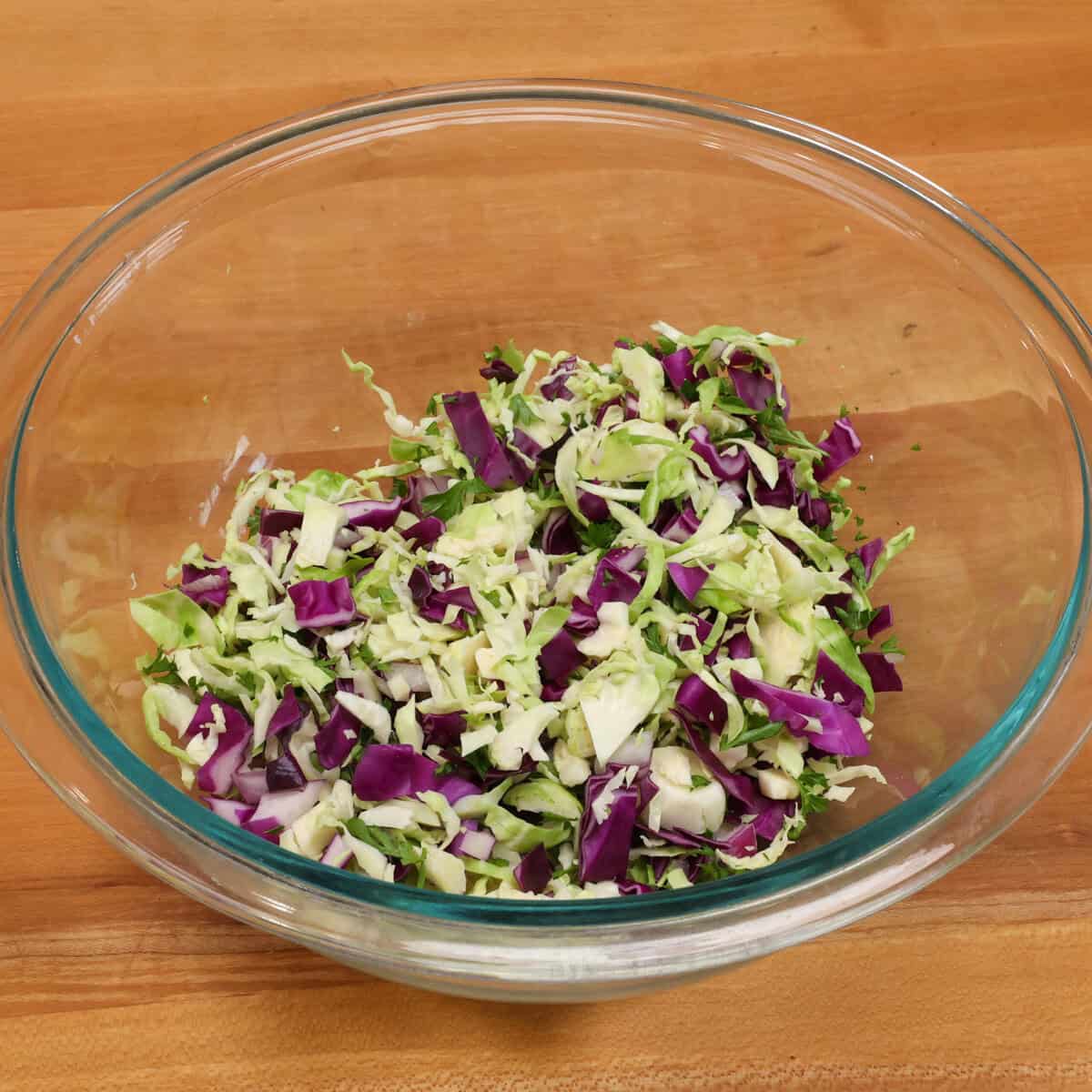 shaved brussels sprouts, chopped cabbage, and other chopped vegetables in a mixing bowl.