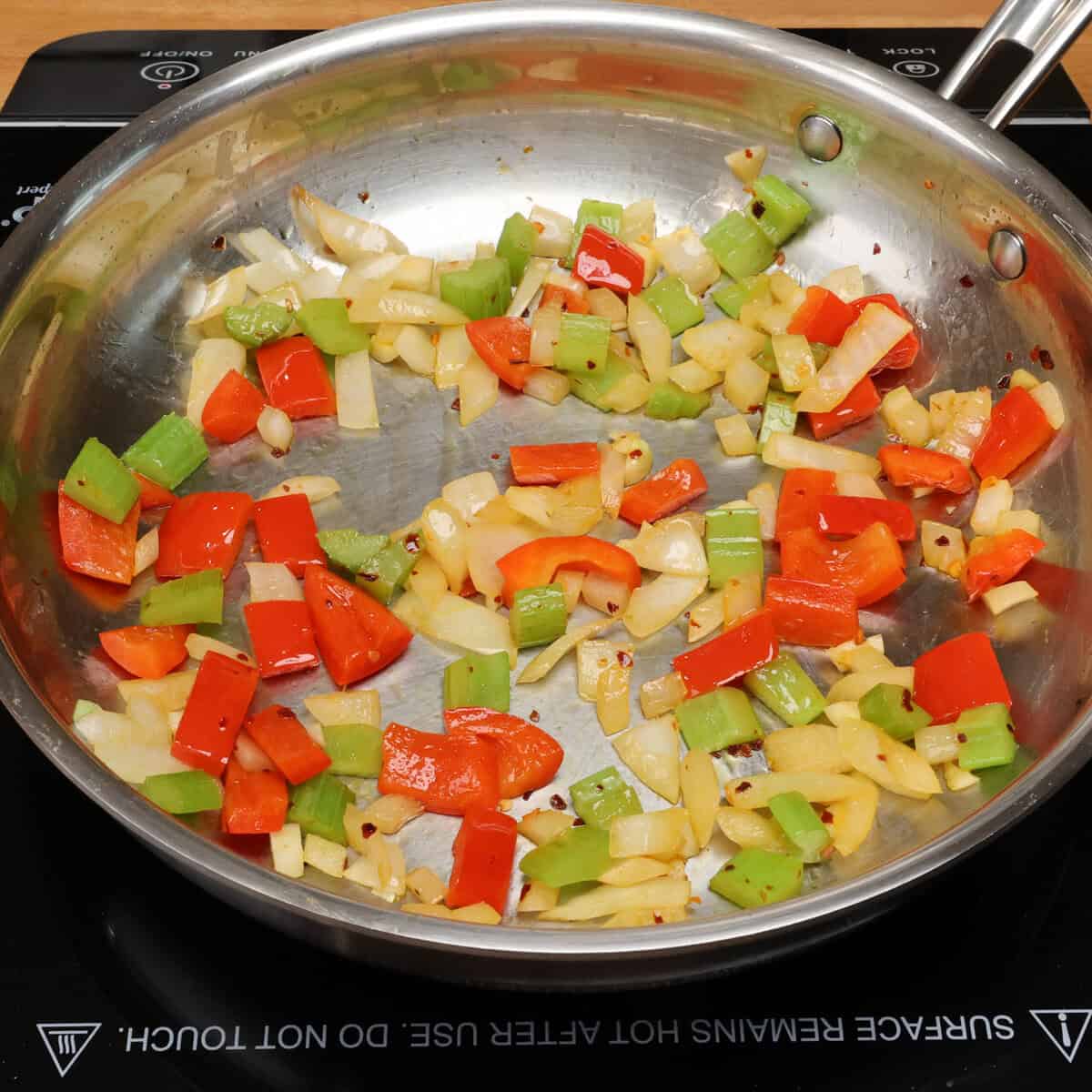 onions, celery, garlic, and chopped red bell peppers cooking in a skillet.