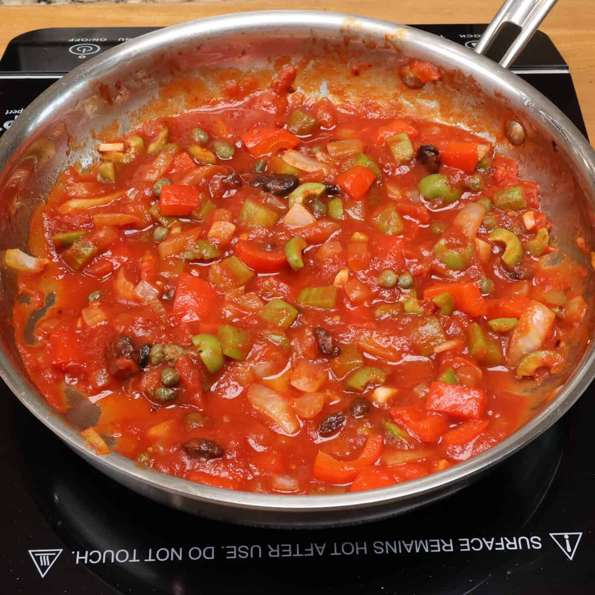 tomato sauce with vegetables and olives simmering in a saucepan.