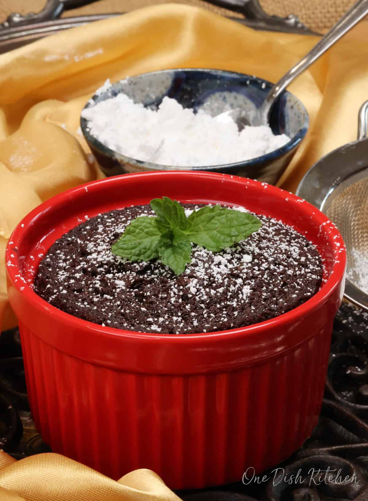 a small chocolate cake topped with powdered sugar in a red ramekin.