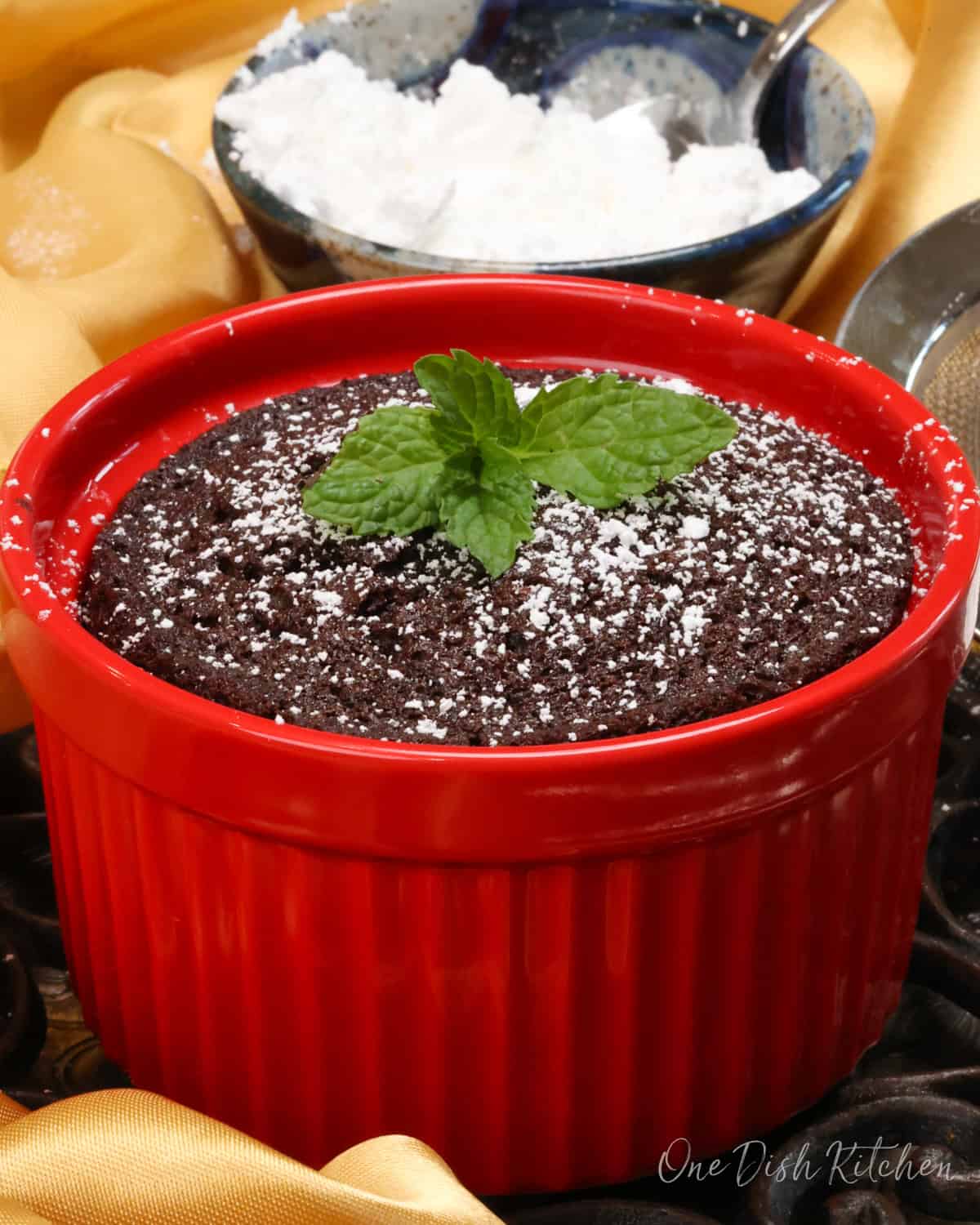 a small chocolate cake topped with powdered sugar in a red ramekin.