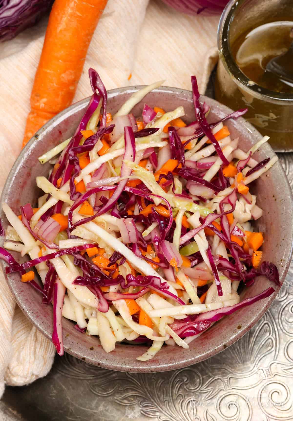a bowl of coleslaw on a silver tray next to a carrot.