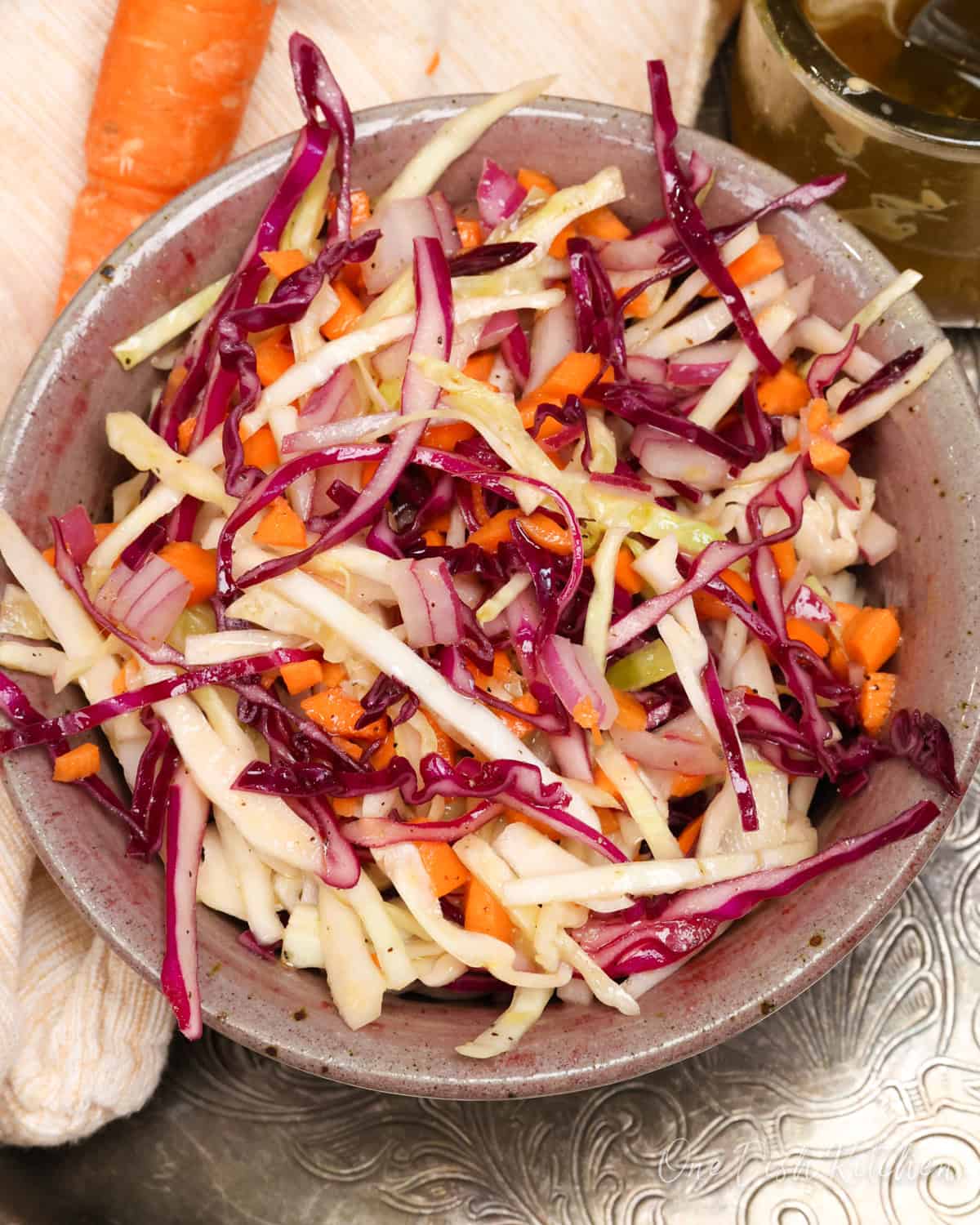 a bowl of coleslaw on a silver tray next to a carrot.