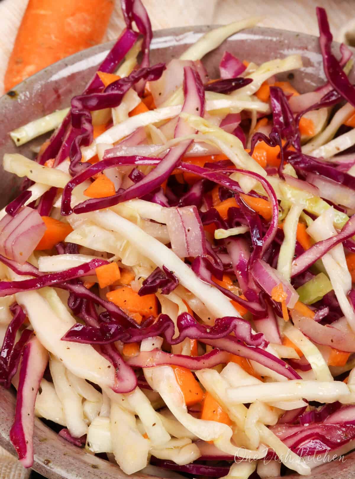 a closeup picture of a bowl of coleslaw in a vinegar based dressing.
