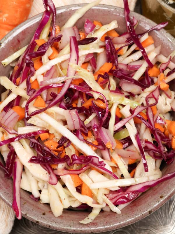 a bowl of coleslaw on a silver tray next to a carrot.