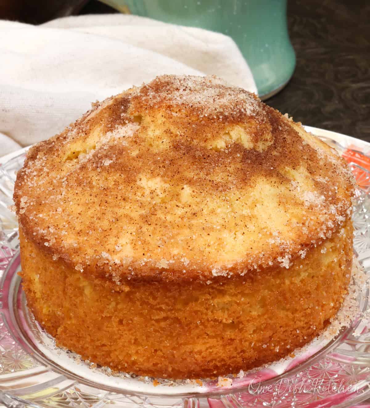 a single French breakfast puff on a white plate next to a cup of coffee.