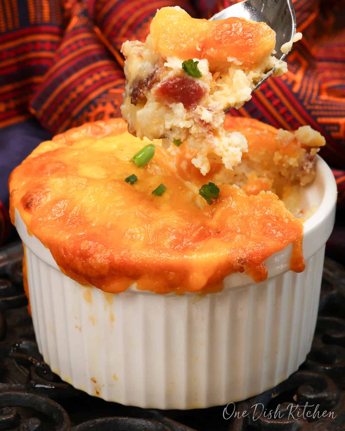 a mini twice baked potato casserole in a small ramekin with a fork on the side.