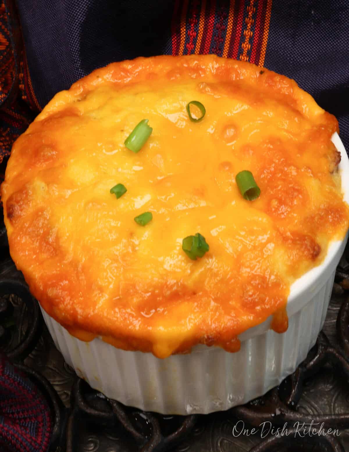 a small loaded twice baked potato casserole in a white ramekin with melted cheddar cheese on the sides.