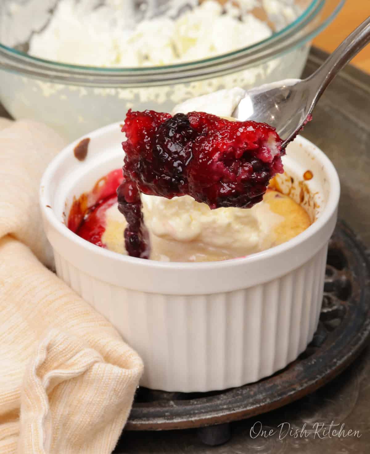 a blackberry cobbler topped with whipped cream and a spoon on the side of the dish.